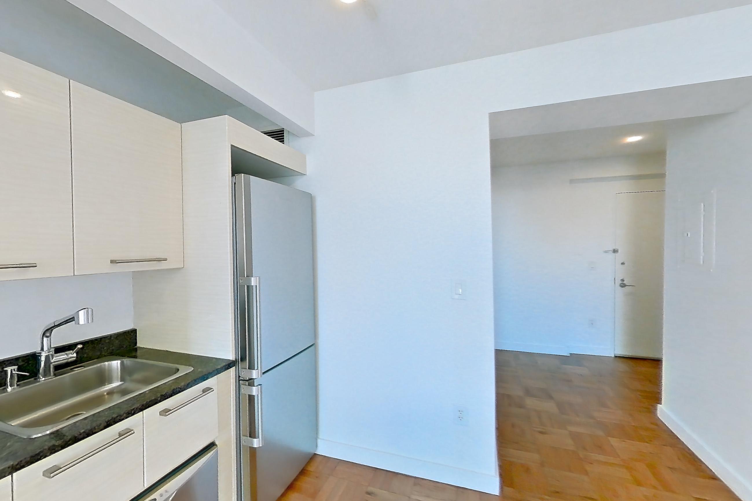 Kitchen with dark stone countertops, dishwasher, gas range, light countertops, light wood-finish flooring, microwave, oven/range, parquet flooring, refrigerator, stainless steel appliances, and white appliances, Apartment 2906 at 20 Exchange Place