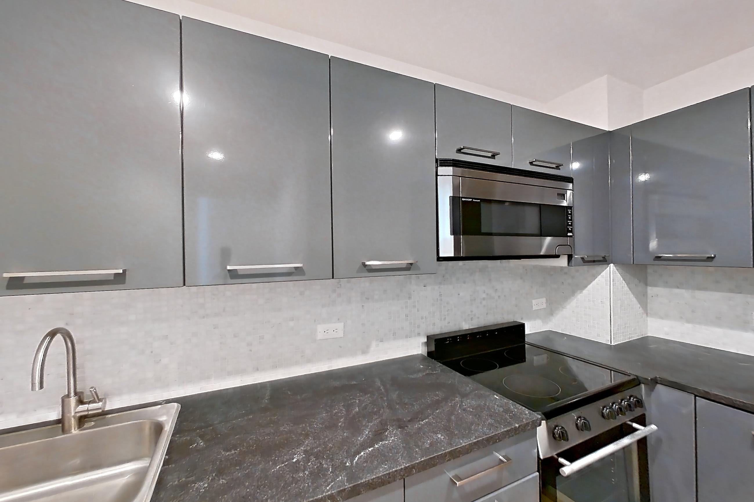 Kitchen with dark countertops, dark stone countertops, electric range, light wood-finish flooring, microwave, refrigerator, and stainless steel appliances, Apartment 1503 at 20 Exchange Place