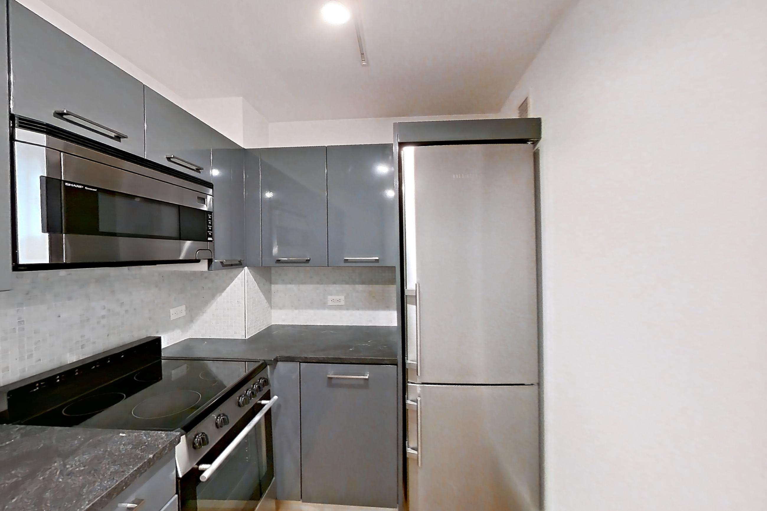 Kitchen with dark countertops, dark stone countertops, electric range, light wood-finish flooring, microwave, refrigerator, and stainless steel appliances, Apartment 1503 at 20 Exchange Place