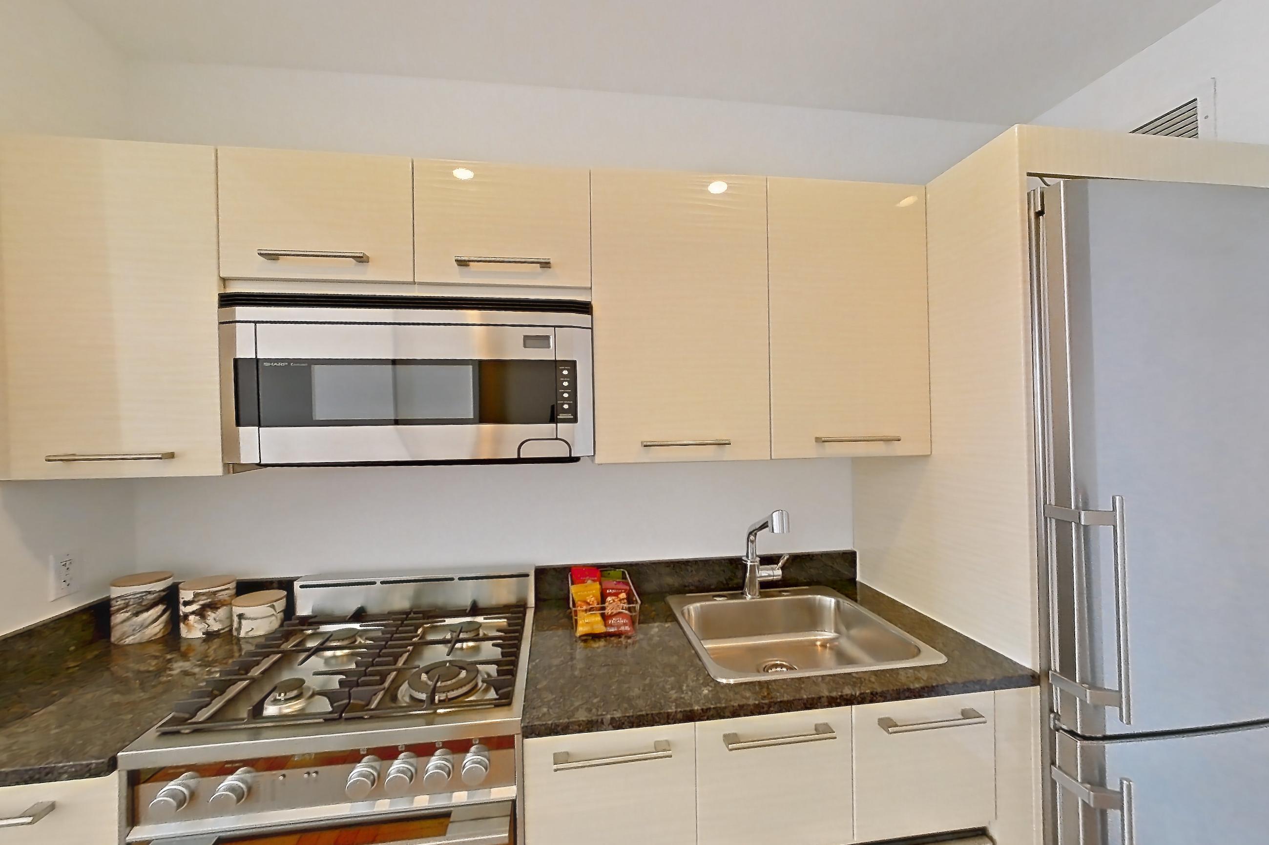 Kitchen with dark stone countertops, dishwasher, gas range, light countertops, light wood-finish flooring, microwave, oven/range, parquet flooring, refrigerator, and stainless steel appliances, Apartment 3006 at 20 Exchange Place