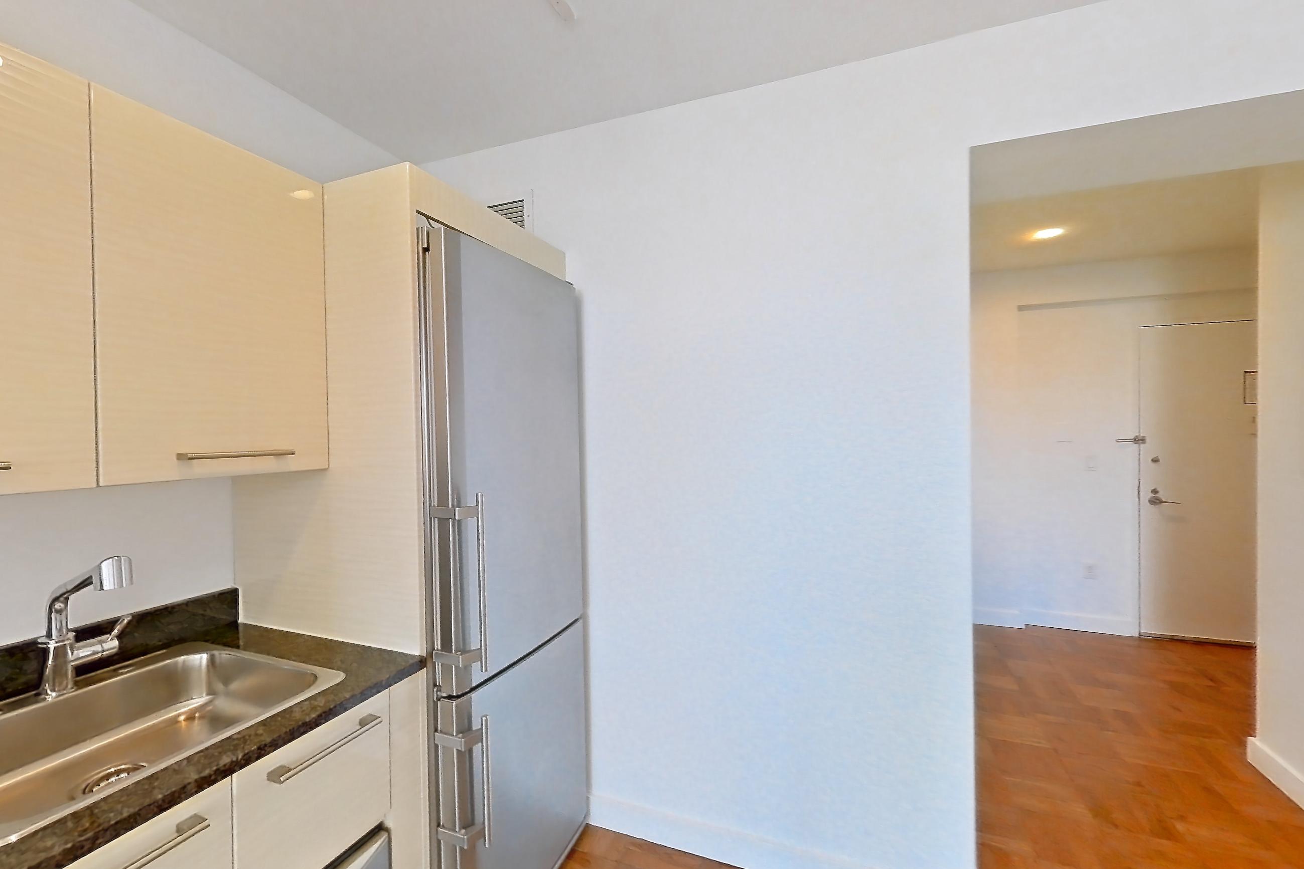 Kitchen with dark stone countertops, dishwasher, gas range, light countertops, light wood-finish flooring, microwave, oven/range, parquet flooring, refrigerator, and stainless steel appliances, Apartment 3006 at 20 Exchange Place