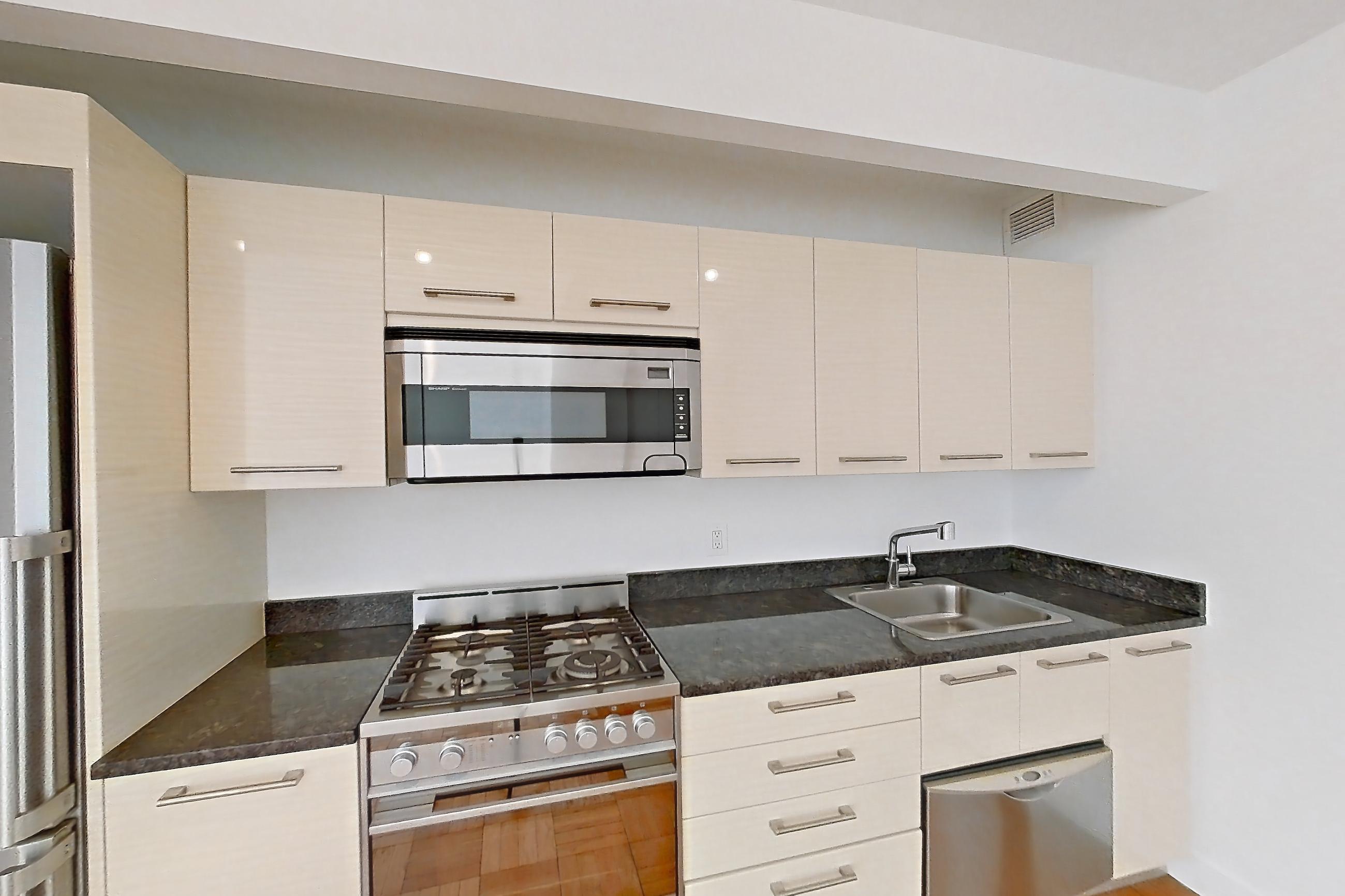 Kitchen with dark countertops, dark stone countertops, dishwasher, gas range, light countertops, light wood-finish flooring, microwave, oven/range, parquet flooring, refrigerator, stainless steel appliances, and white appliances, Apartment 2104 at 20 Exchange Place