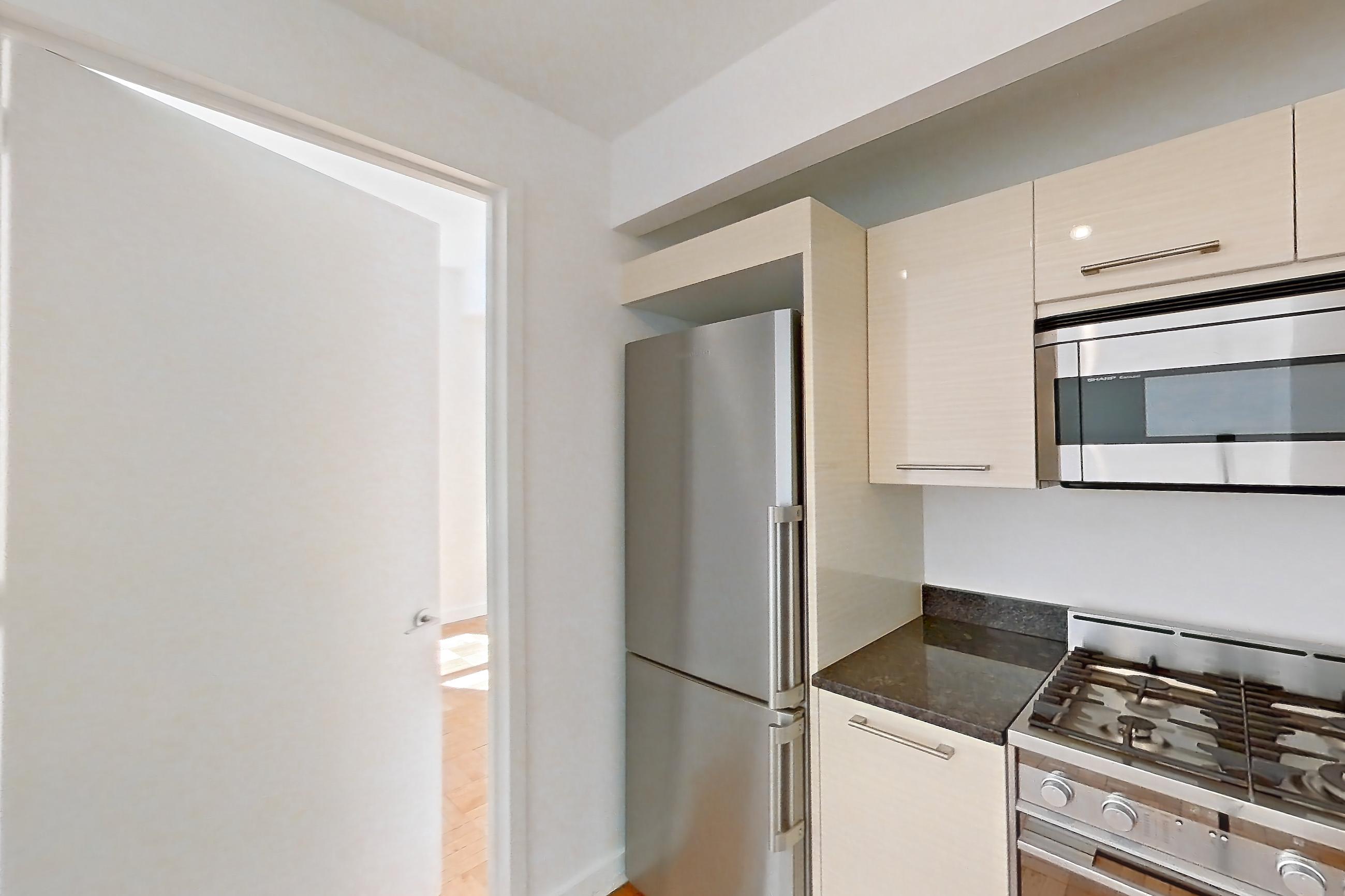 Kitchen with dark countertops, dark stone countertops, dishwasher, gas range, light countertops, light wood-finish flooring, microwave, oven/range, parquet flooring, refrigerator, stainless steel appliances, and white appliances, Apartment 2104 at 20 Exchange Place
