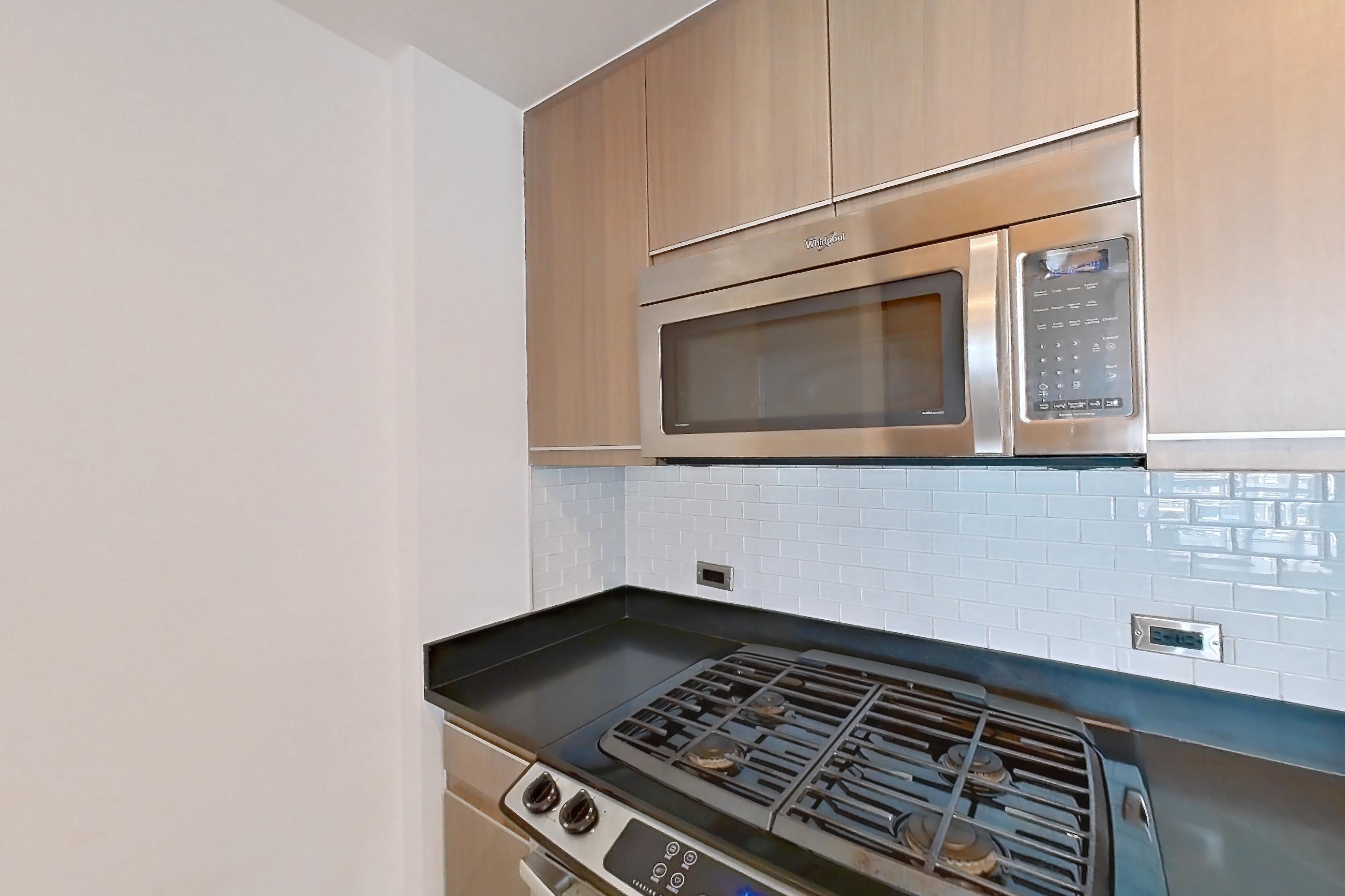 Kitchen with dark countertops, dishwasher, gas range, light tile flooring, microwave, oven/range, refrigerator, and stainless steel appliances, Apartment 25A at 66 Rockwell