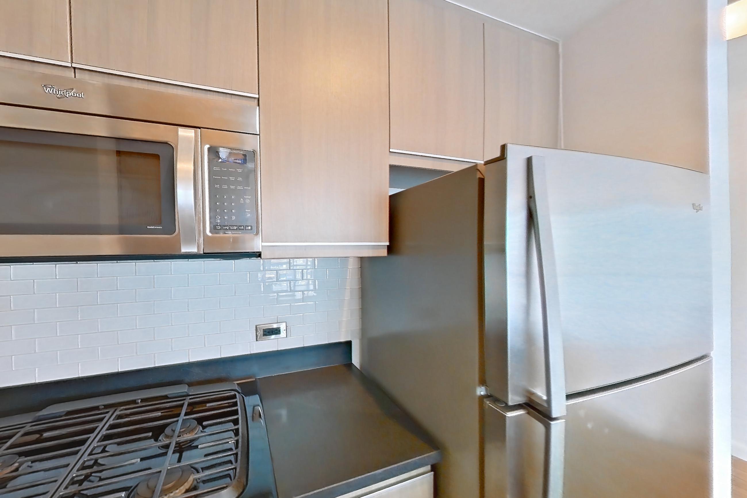 Kitchen with dark countertops, dishwasher, gas range, light tile flooring, microwave, oven/range, refrigerator, and stainless steel appliances, Apartment 25A at 66 Rockwell