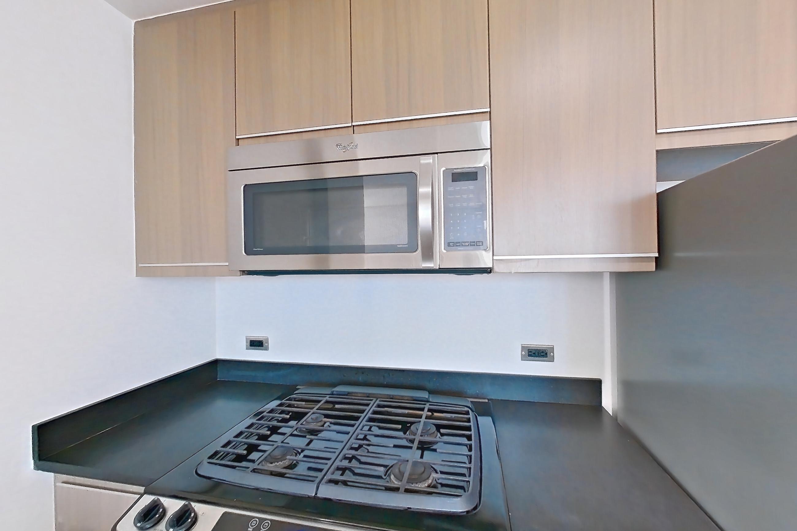 Kitchen with dark countertops, dark tile flooring, dishwasher, gas range, light countertops, light tile flooring, microwave, oven/range, refrigerator, and stainless steel appliances, Apartment 18J at 66 Rockwell