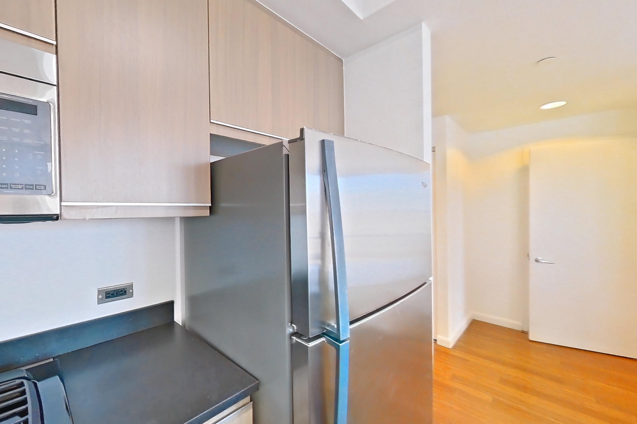 Kitchen with dark countertops, dark tile flooring, dishwasher, gas range, light countertops, light tile flooring, microwave, oven/range, refrigerator, and stainless steel appliances, Apartment 18J at 66 Rockwell