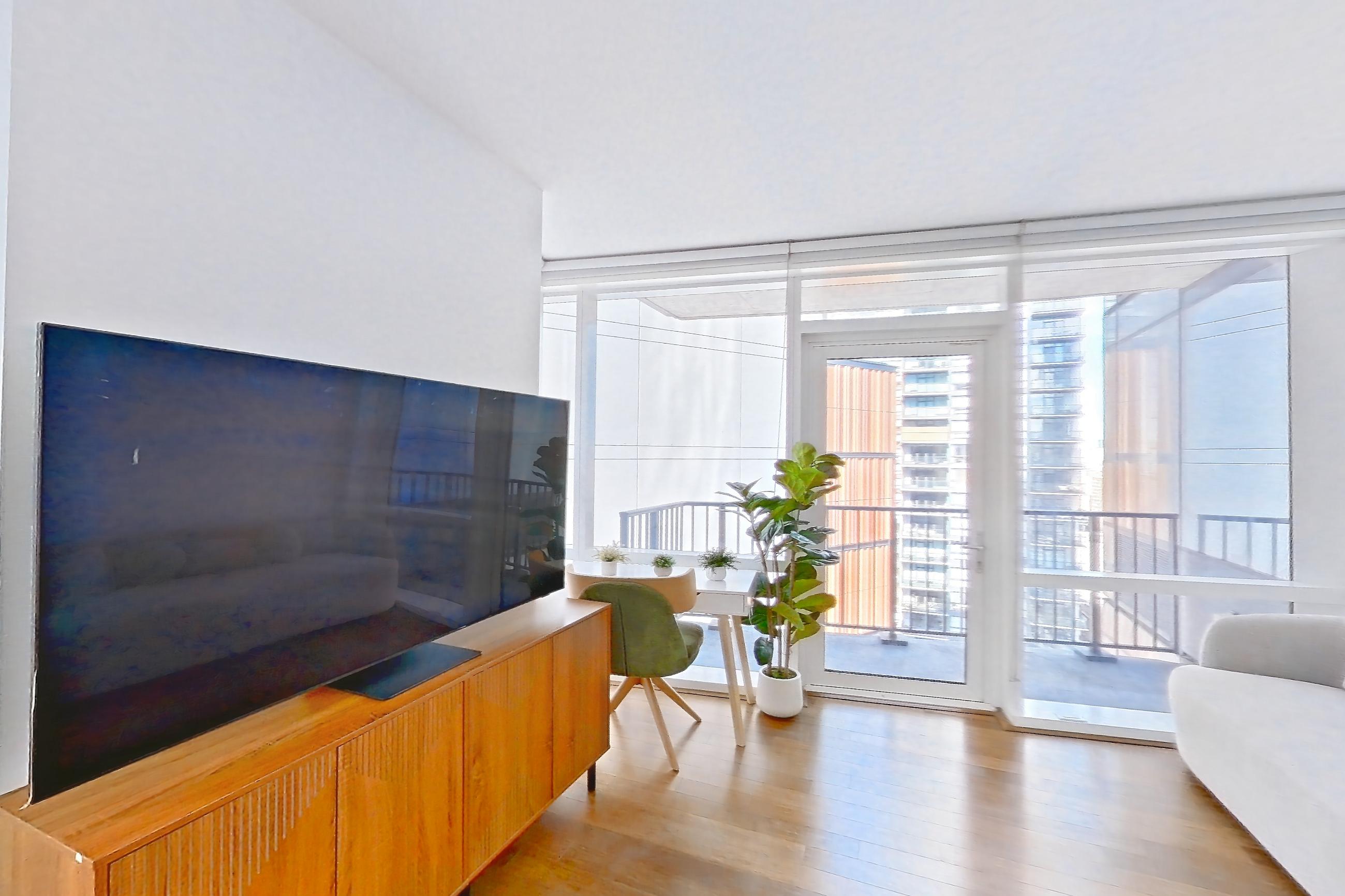 Living room with light wood-finish flooring, refrigerator, and stainless steel appliances, Apartment 18J at 66 Rockwell