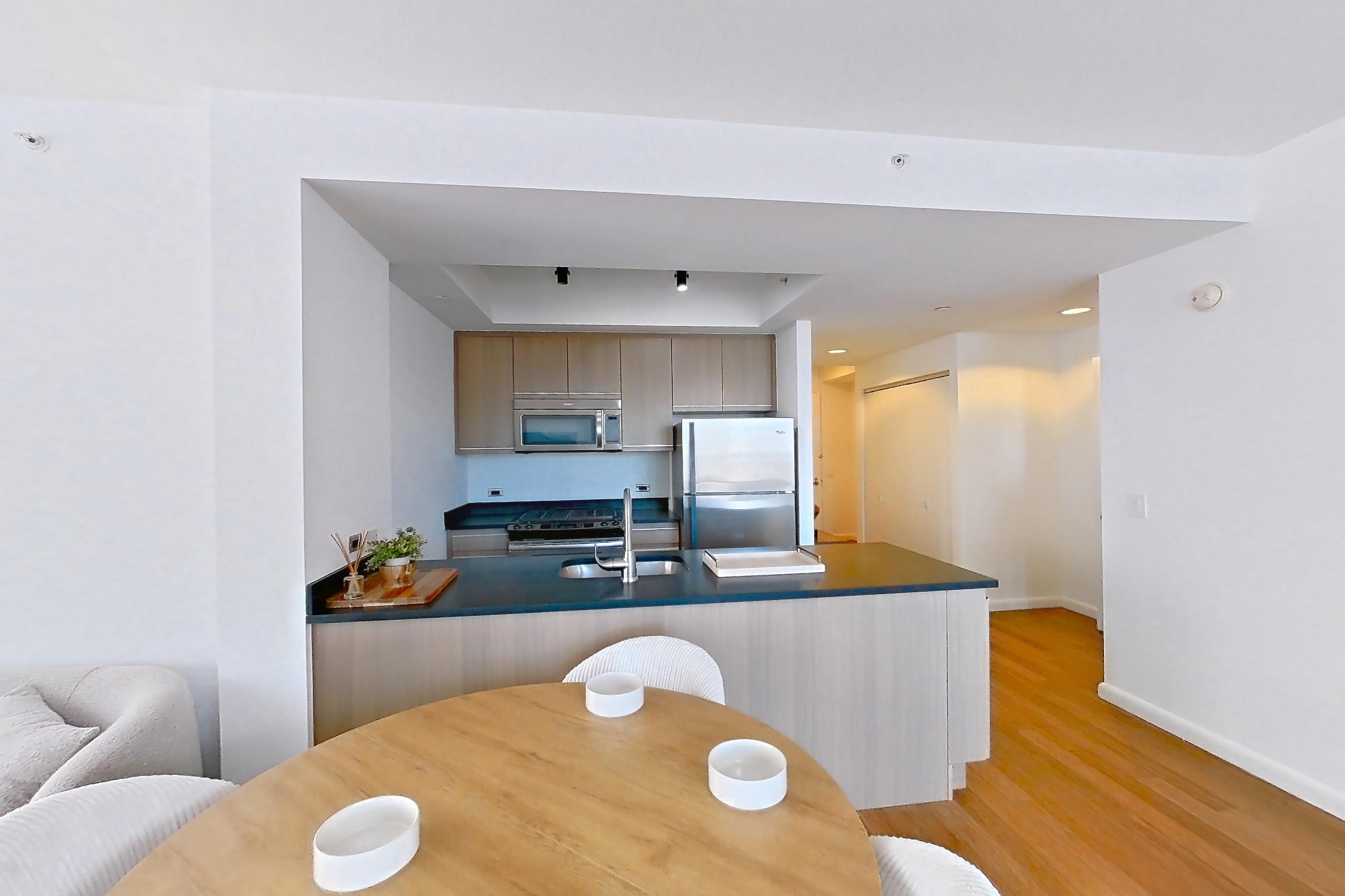 Living room with light wood-finish flooring, refrigerator, and stainless steel appliances, Apartment 18J at 66 Rockwell