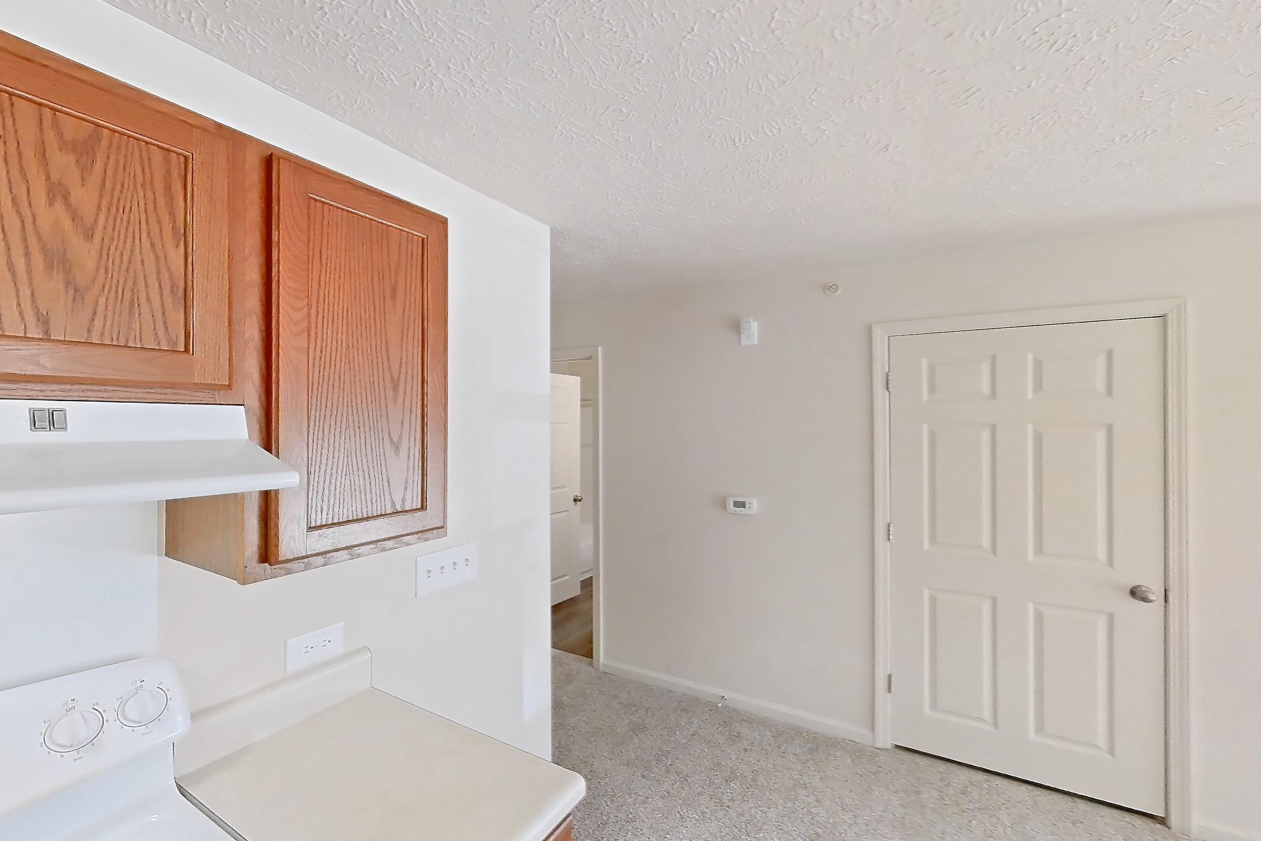 Kitchen with dishwasher, electric range, light carpet, light countertops, light wood-finish flooring, oven/range, refrigerator, and white appliances, Apartment 412 at Village Park