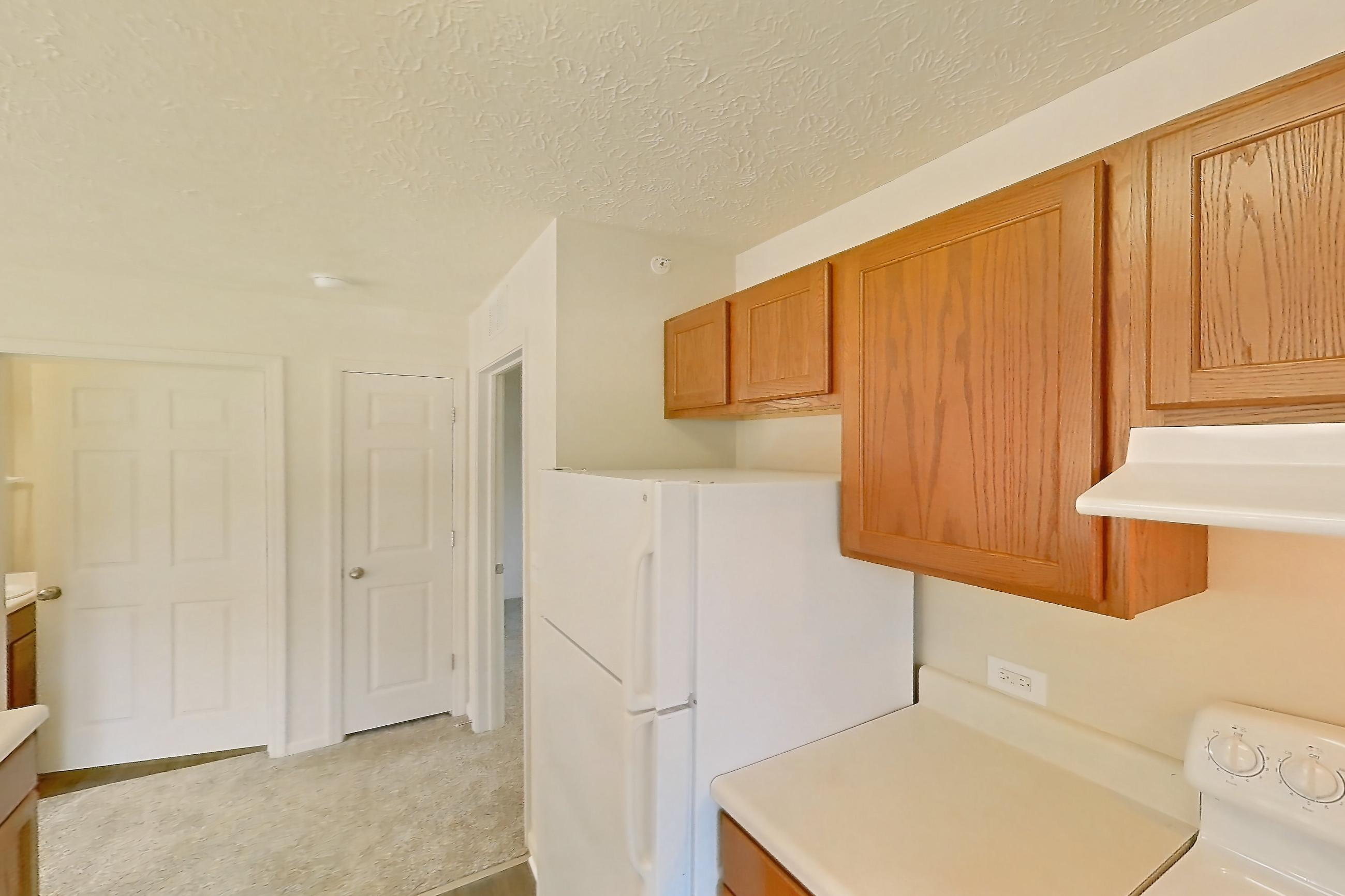 Kitchen with dark wood-finish flooring, dishwasher, electric range, light countertops, light wood-finish flooring, oven/range, range hood, refrigerator, and white appliances, Apartment 418 at Village Park