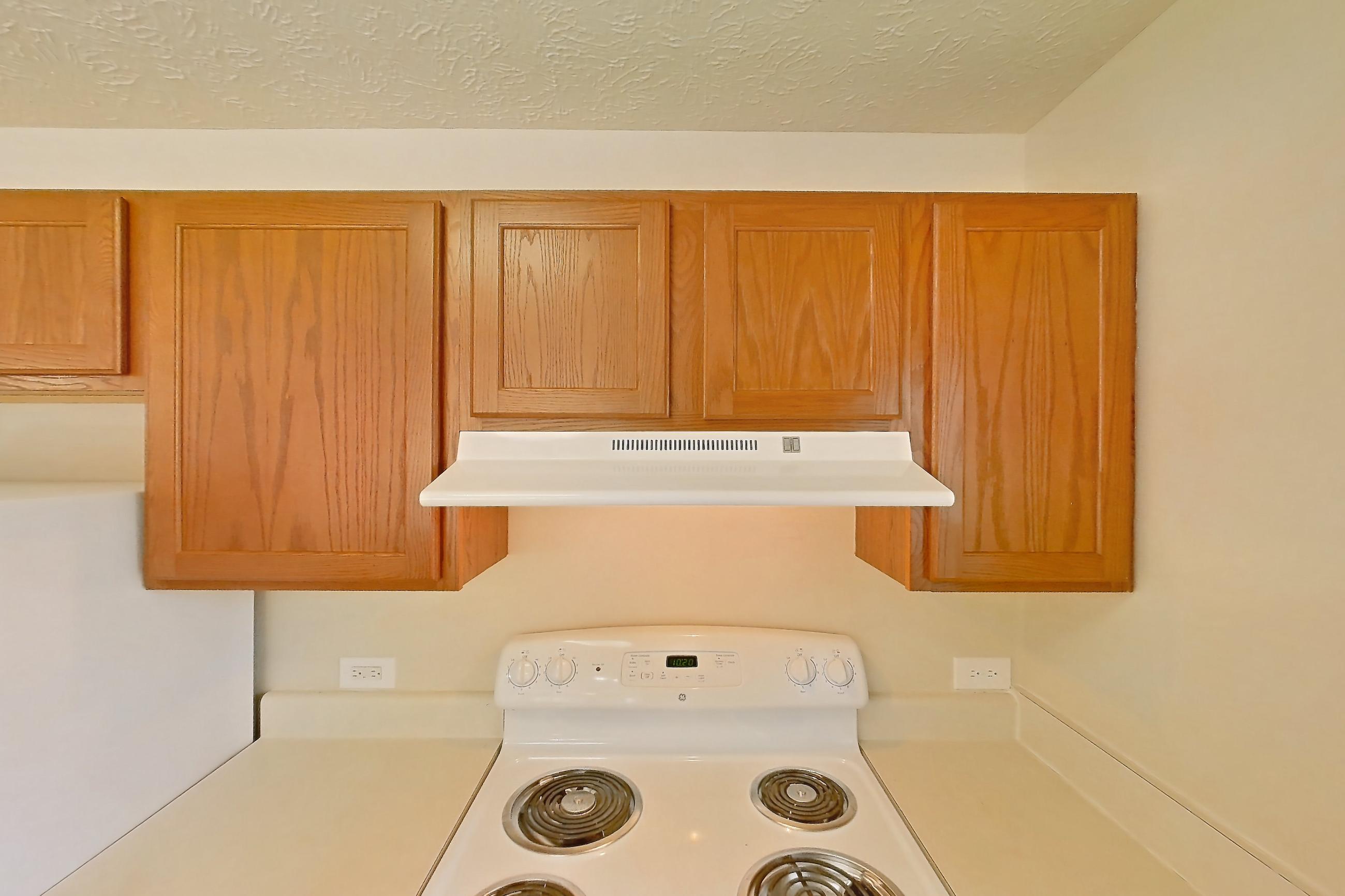 Kitchen with dark wood-finish flooring, dishwasher, electric range, light countertops, light wood-finish flooring, oven/range, range hood, refrigerator, and white appliances, Apartment 418 at Village Park