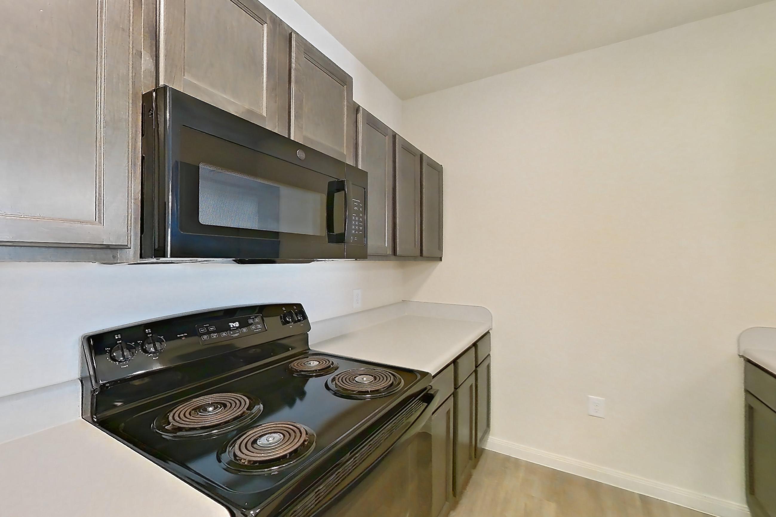 Kitchen with black appliances, dishwasher, electric range, light countertops, light wood-finish flooring, oven/range, refrigerator, and stainless steel appliances, Apartment 11203 at Crosswinds