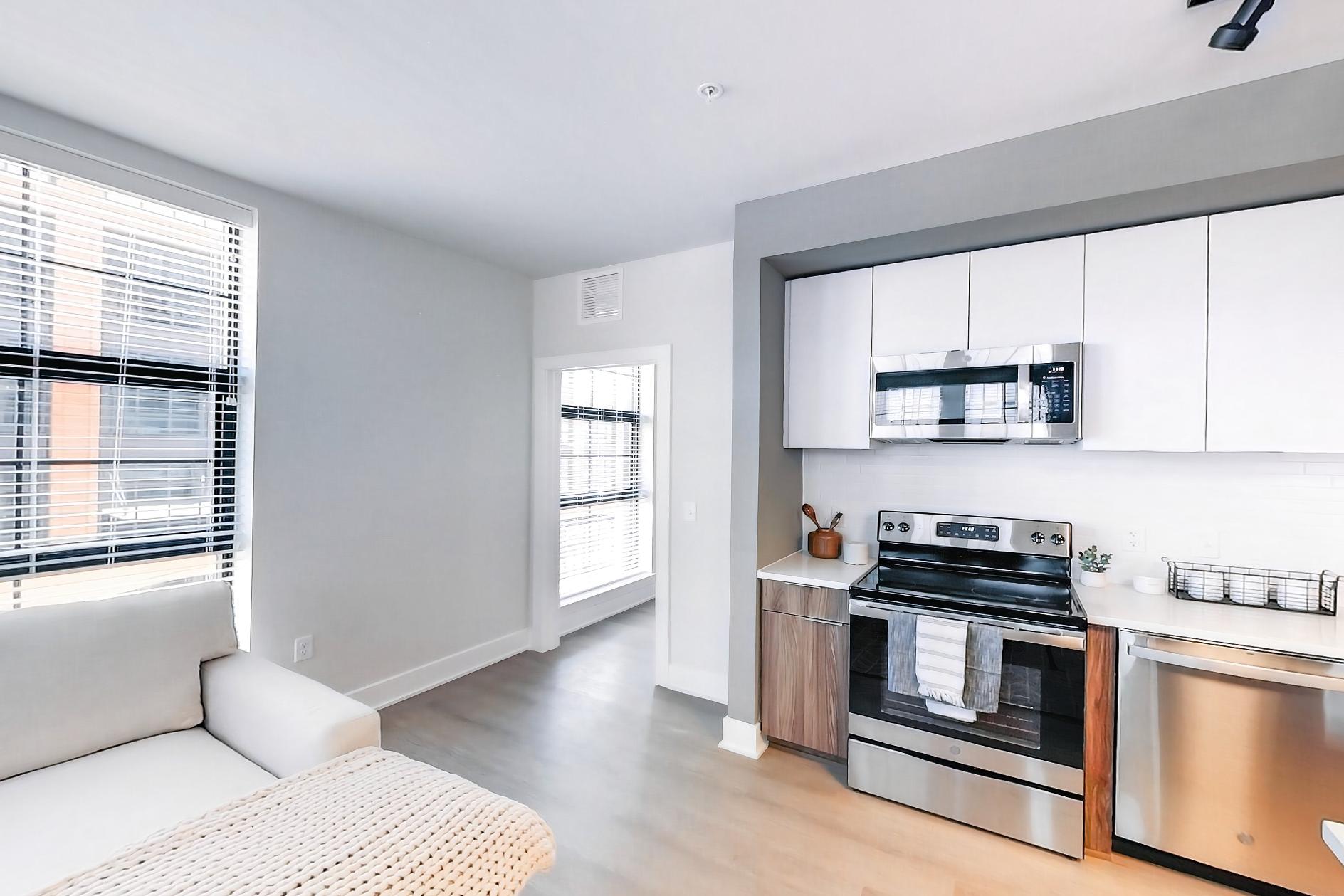Living space with dishwasher, electric range, light stone countertops, light wood-finish flooring, microwave, oven/range, and stainless steel appliances, Apartment L3 Model at Rye House