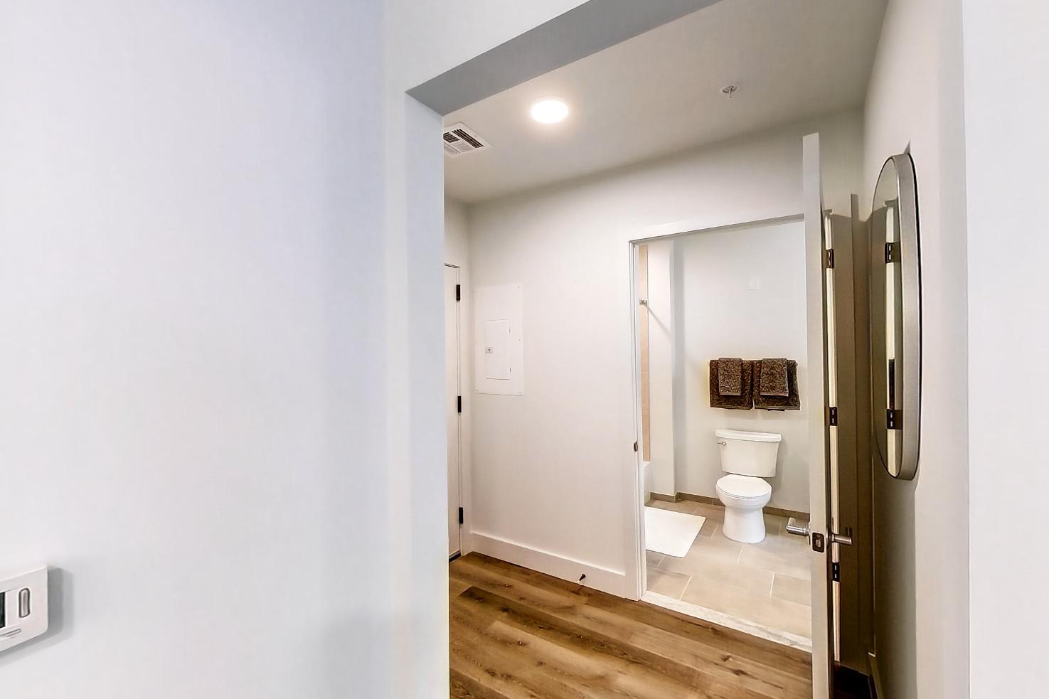 Kitchen entryway with dark wood-finish flooring, dishwasher, electric range, light countertops, light stone countertops, light wood-finish flooring, microwave, oven/range, refrigerator, and stainless steel appliances, Apartment Model at 250 Mission
