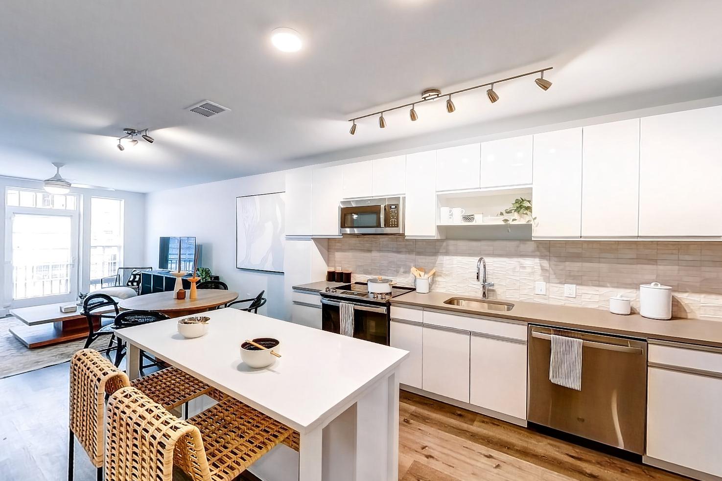 Kitchen entryway with dark wood-finish flooring, dishwasher, electric range, light countertops, light stone countertops, light wood-finish flooring, microwave, oven/range, refrigerator, and stainless steel appliances, Apartment Model at 250 Mission