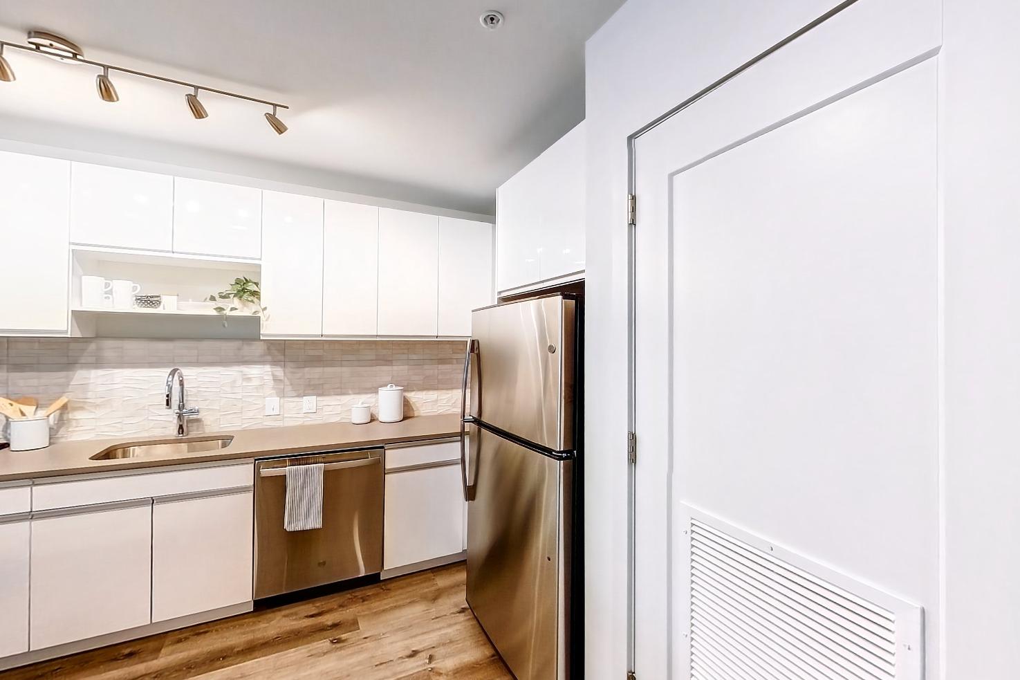Kitchen entryway with dark wood-finish flooring, dishwasher, electric range, light countertops, light stone countertops, light wood-finish flooring, microwave, oven/range, refrigerator, and stainless steel appliances, Apartment Model at 250 Mission