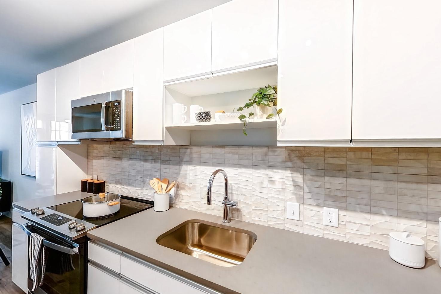 Kitchen with dishwasher, electric range, light countertops, light stone countertops, light wood-finish flooring, microwave, oven/range, and stainless steel appliances, Apartment Model at 250 Mission